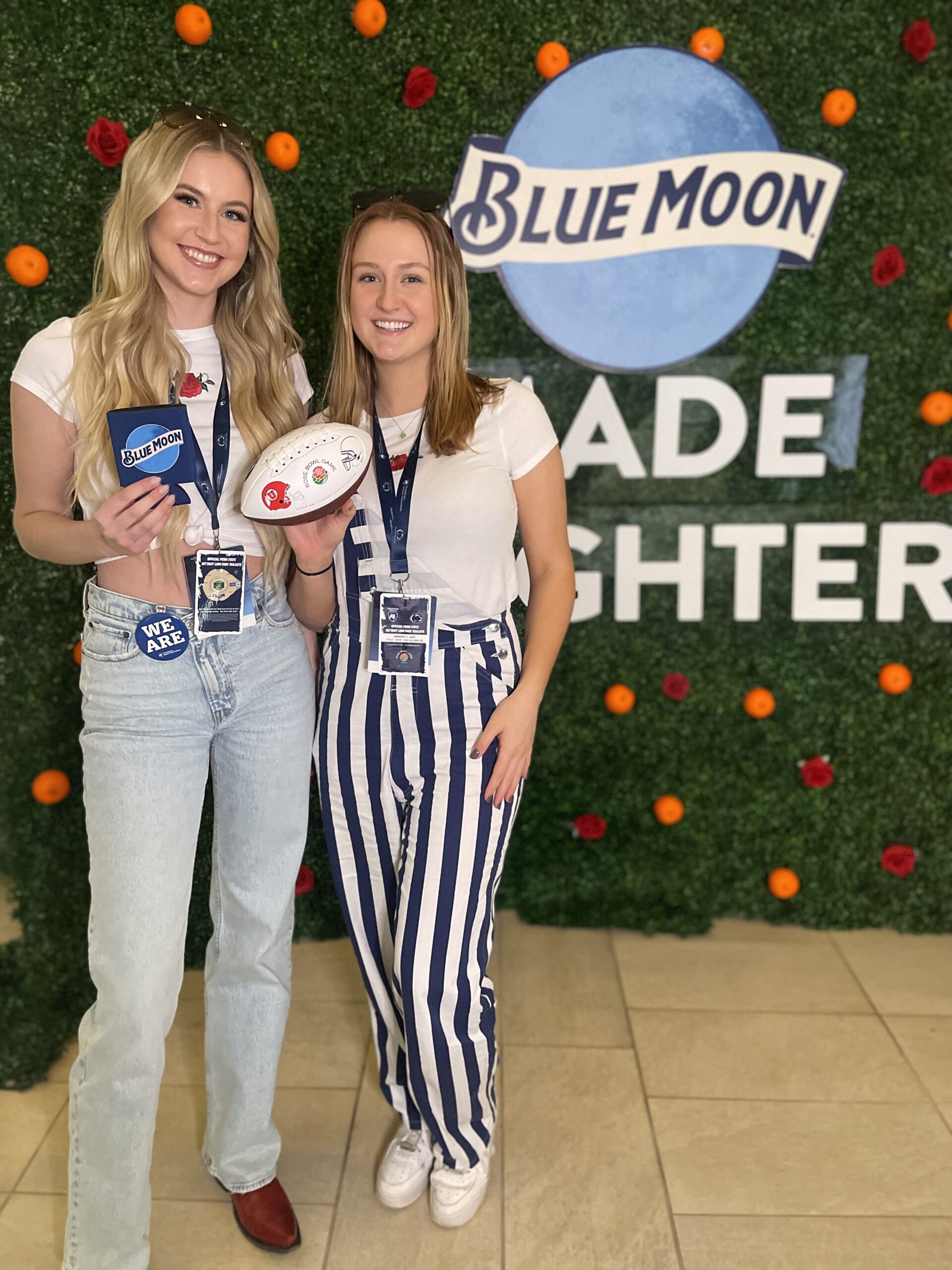 Two women holding custom photo booth props in front of custom backdrop