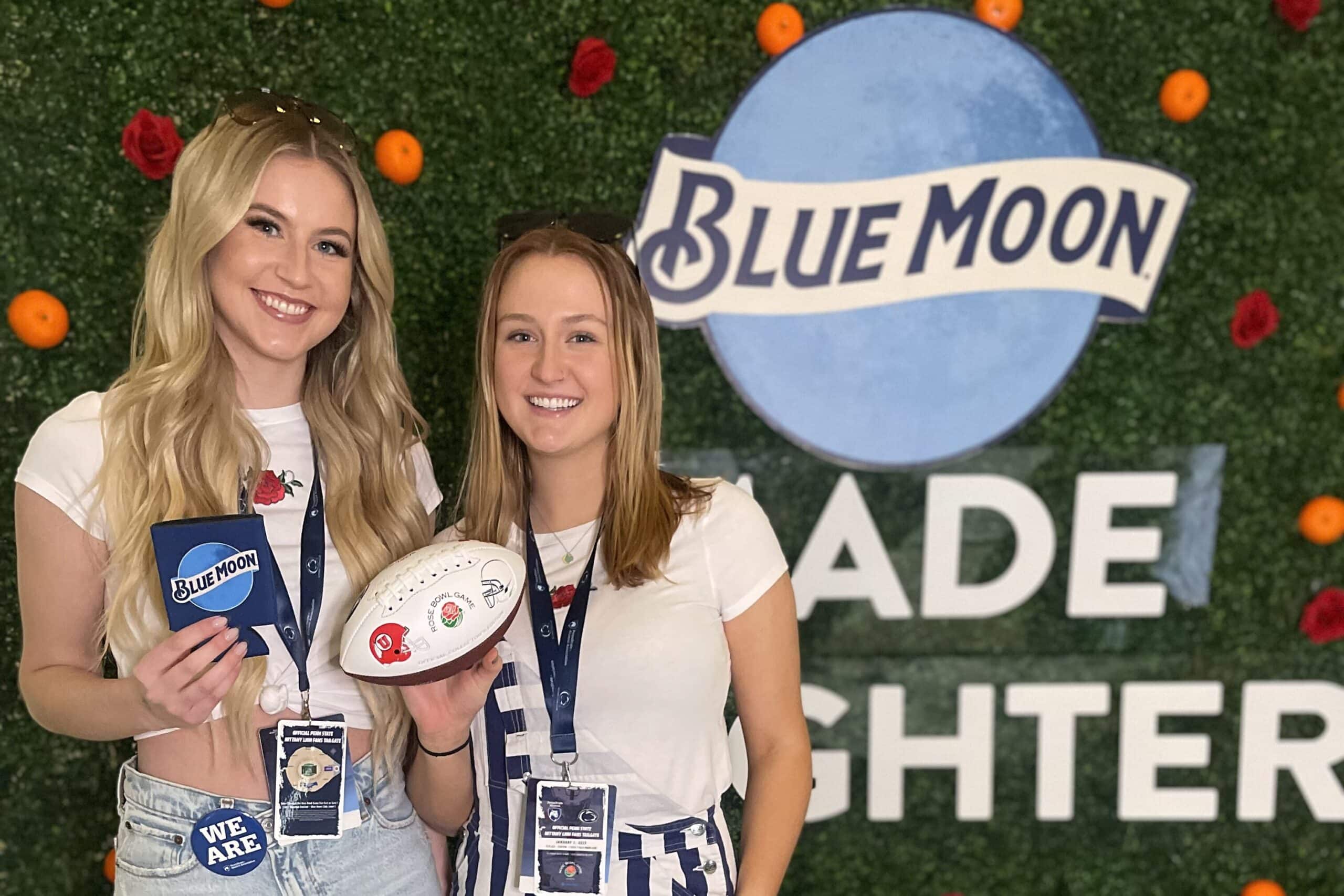Two women holding custom photo booth props in front of custom backdrop