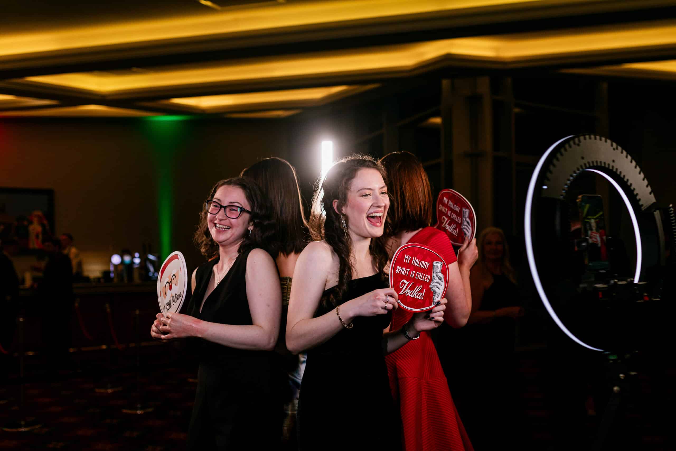 Ladies enjoying having their photos taken at a party by the 360 booth, holding signboards